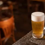 Jarra de cerveza rubia con espuma sobre una mesa de madera en un bar
